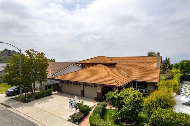 view of front facade featuring a tiled roof, an attached garage, driveway, and a chimney