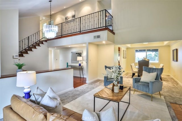 living area with visible vents, an inviting chandelier, a towering ceiling, stairway, and carpet