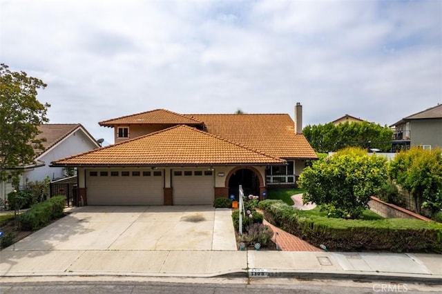mediterranean / spanish home featuring an attached garage, concrete driveway, a tiled roof, and a chimney