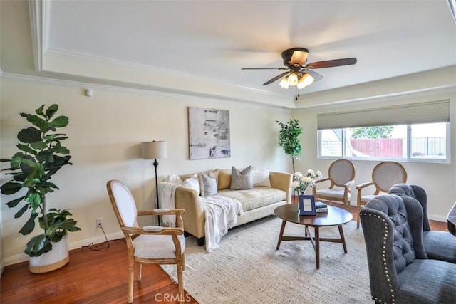 living room featuring crown molding, wood finished floors, baseboards, a raised ceiling, and a ceiling fan