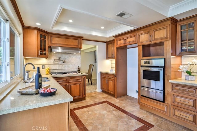 kitchen with brown cabinetry, crown molding, appliances with stainless steel finishes, a warming drawer, and under cabinet range hood