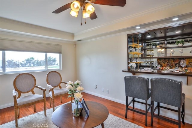 sitting room featuring bar, a ceiling fan, wood finished floors, baseboards, and ornamental molding