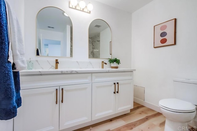 full bathroom with visible vents, toilet, wood finished floors, a sink, and double vanity