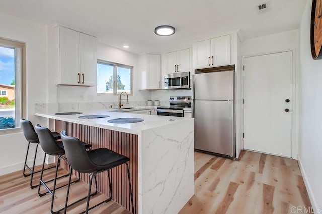 kitchen with a peninsula, a kitchen bar, stainless steel appliances, light wood finished floors, and a sink