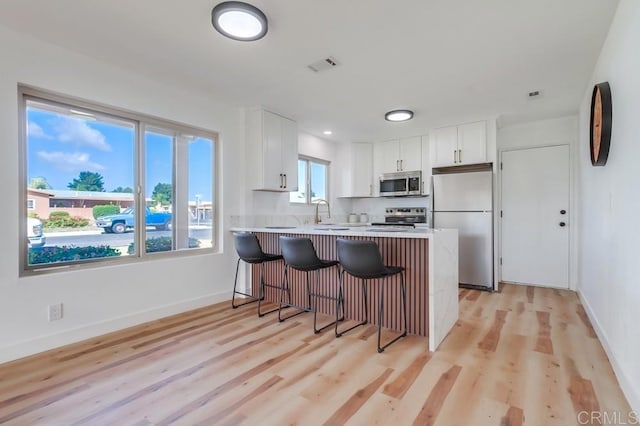 kitchen featuring a peninsula, visible vents, light countertops, stainless steel appliances, and a breakfast bar area