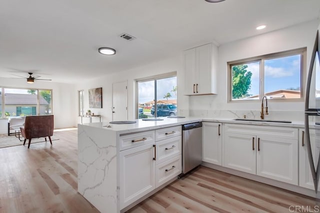 kitchen with a sink, dishwasher, white cabinets, a peninsula, and visible vents