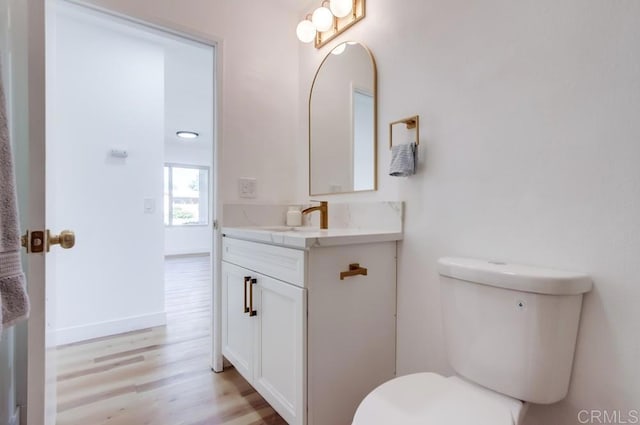 bathroom with toilet, vanity, wood finished floors, and baseboards
