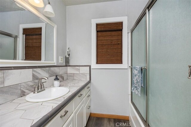 3432 N Arrowhead Ave, San Bernardino, CA 92405 - bathroom featuring wood finished floors, vanity, decorative backsplash, bath / shower combo with glass door, and baseboards