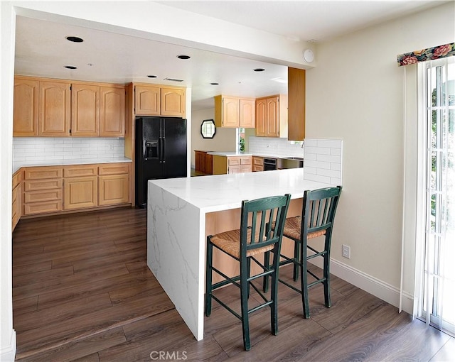 kitchen with dark wood finished floors, light brown cabinetry, black appliances, a peninsula, and tasteful backsplash