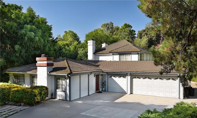 view of front of home with concrete driveway, a tile roof, a chimney, and stucco siding