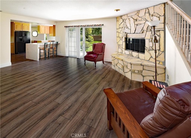 living area featuring a stone fireplace, baseboards, dark wood-type flooring, and stairway