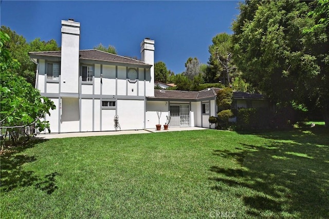rear view of property with a lawn, a chimney, and stucco siding