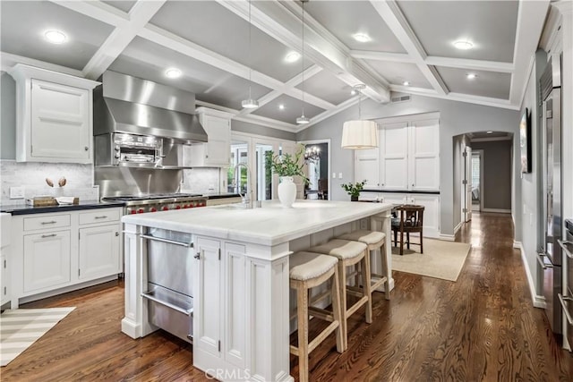 kitchen with a warming drawer, arched walkways, wall chimney exhaust hood, and dark wood-style flooring