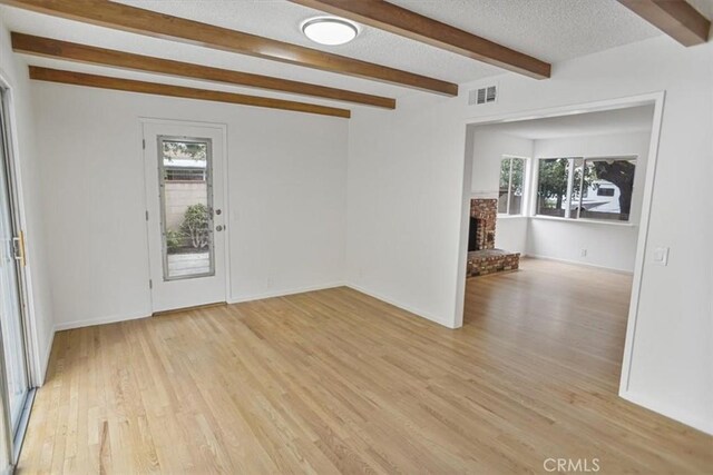 6833 Sultana Ave, San Gabriel, CA 91775 - empty room featuring beamed ceiling, plenty of natural light, light wood-type flooring, a fireplace, and a textured ceiling