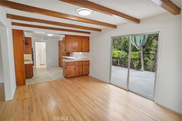 6833 Sultana Ave, San Gabriel, CA 91775 - kitchen featuring beamed ceiling, light countertops, brown cabinetry, light wood-style floors, and a textured ceiling