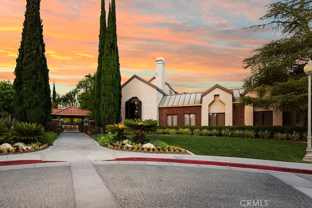 mediterranean / spanish-style home with a chimney, stucco siding, brick siding, a gazebo, and a front yard