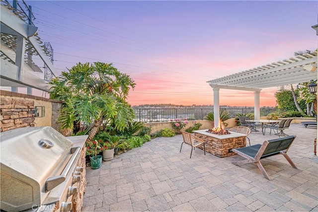 patio terrace at dusk featuring a fire pit, area for grilling, a fenced backyard, and a pergola