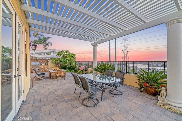 patio terrace at dusk with a fire pit, exterior kitchen, a pergola, and outdoor dining area