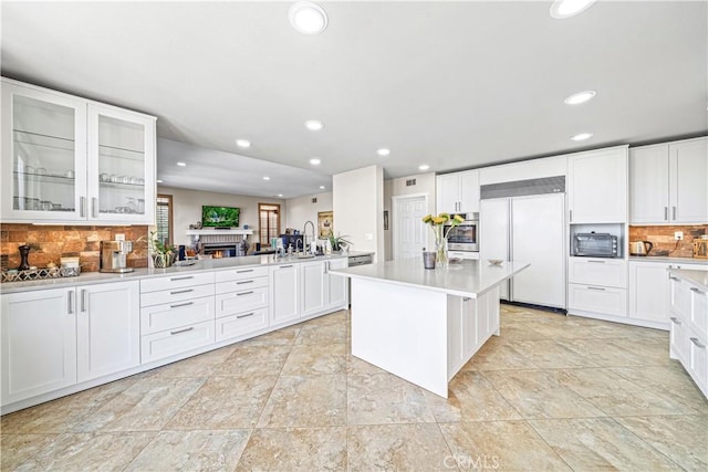 kitchen featuring oven, white cabinetry, built in fridge, and backsplash