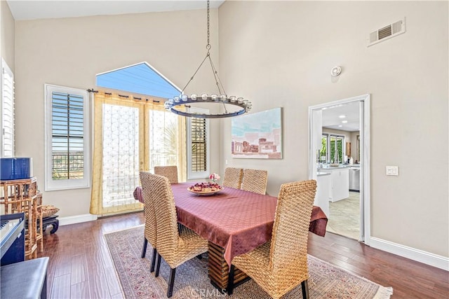 dining area with an inviting chandelier, wood finished floors, visible vents, and high vaulted ceiling