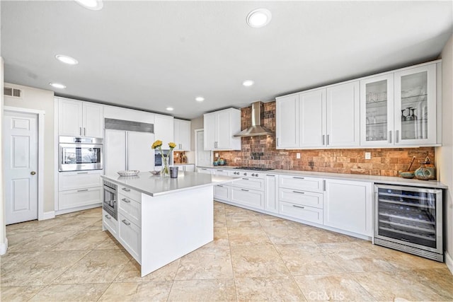kitchen featuring wall chimney range hood, beverage cooler, visible vents, built in appliances, and backsplash