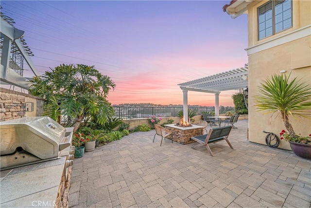 patio terrace at dusk with a grill, an outdoor fire pit, a fenced backyard, and a pergola