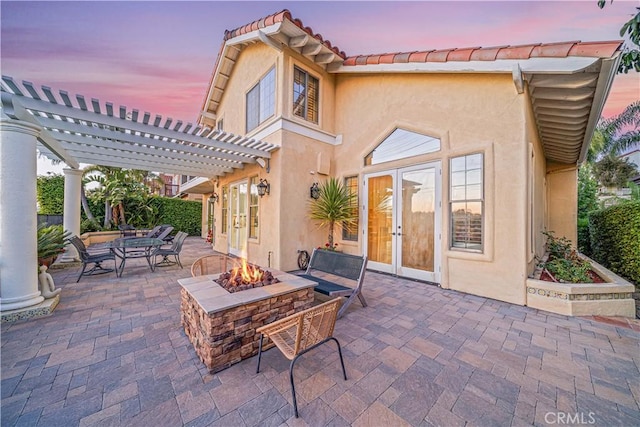 patio terrace at dusk featuring a pergola, a fire pit, and french doors