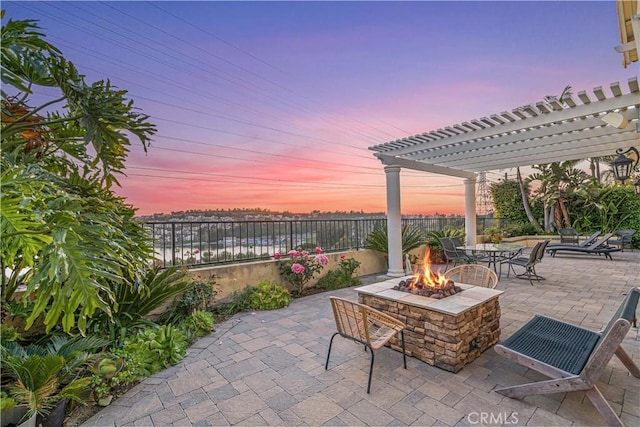 patio terrace at dusk with a fire pit, a pergola, and a fenced backyard