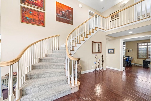 stairs with baseboards, wood finished floors, a baseboard heating unit, and a high ceiling