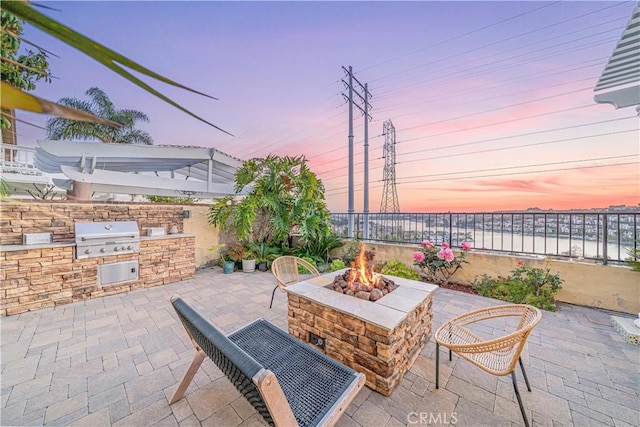 view of patio with exterior kitchen, a fire pit, grilling area, and fence
