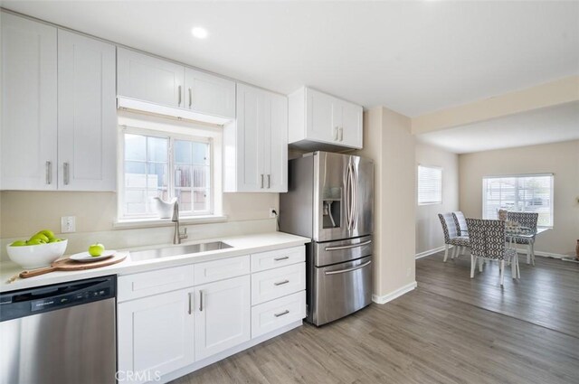 653 Joann St, Costa Mesa, CA 92627 - kitchen with light countertops, white cabinets, a sink, light wood-style flooring, and stainless steel appliances