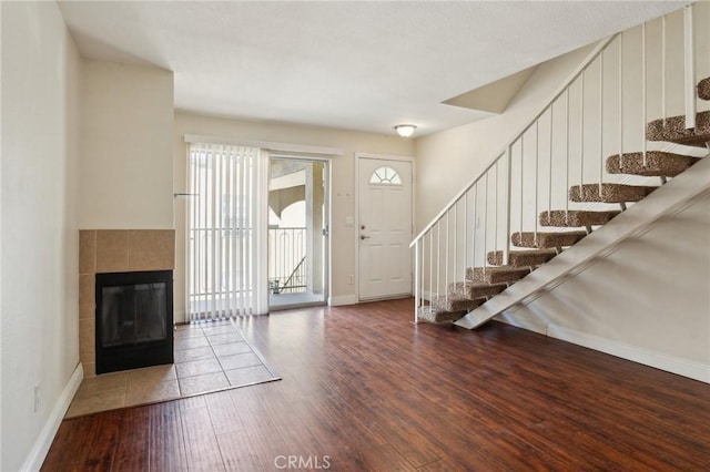 entrance foyer with a tile fireplace, stairs, wood finished floors, and baseboards