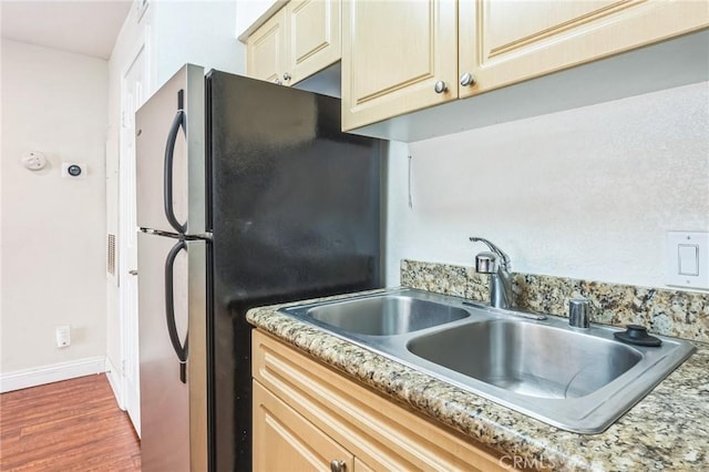 kitchen featuring wood finished floors, a sink, freestanding refrigerator, baseboards, and cream cabinets