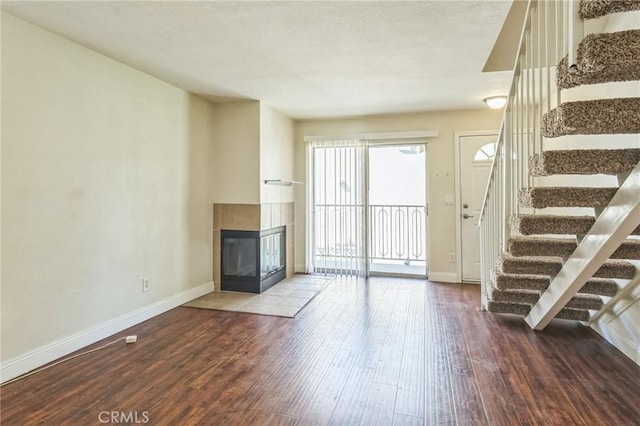 unfurnished living room featuring stairway, baseboards, a tile fireplace, and wood finished floors
