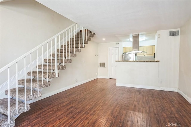 unfurnished living room featuring wood finished floors, visible vents, baseboards, and stairway