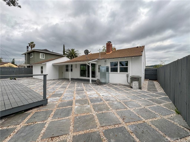 back of house featuring a fenced backyard, a patio, a chimney, and stucco siding