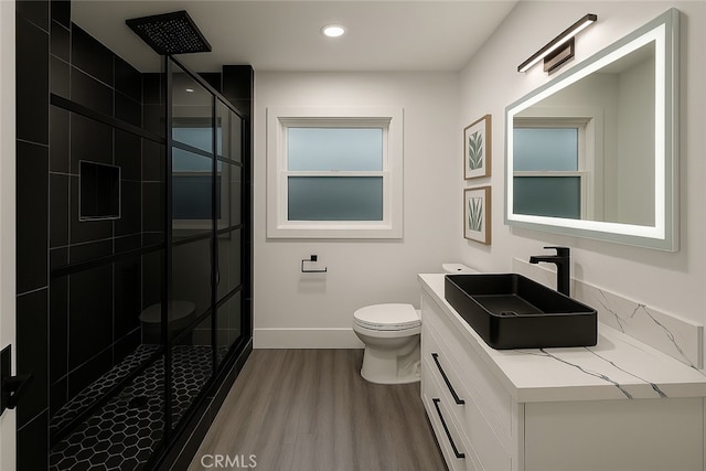 bathroom featuring vanity, wood finished floors, toilet, baseboards, and a stall shower
