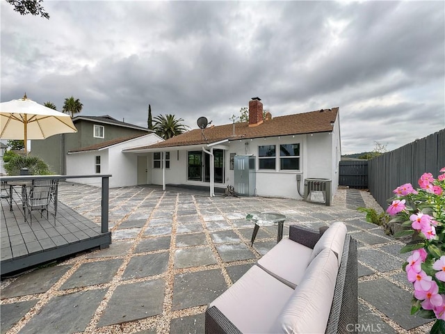 rear view of house with stucco siding, a fenced backyard, a chimney, cooling unit, and a patio area