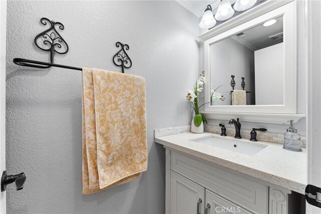 bathroom featuring a textured wall, visible vents, vanity, and ornamental molding