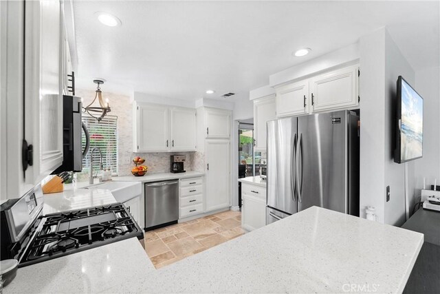 kitchen with light stone counters, a sink, stone tile flooring, stainless steel appliances, and white cabinets