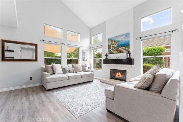 living area featuring wood finished floors, a glass covered fireplace, high vaulted ceiling, and a healthy amount of sunlight