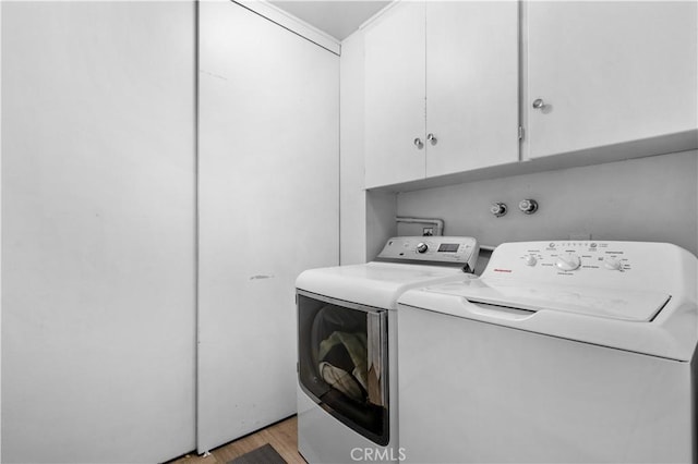 washroom featuring light wood-type flooring, washer and clothes dryer, and cabinet space
