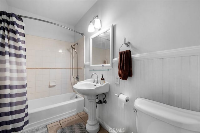 bathroom featuring shower / bath combination with curtain, toilet, a wainscoted wall, and tile patterned floors
