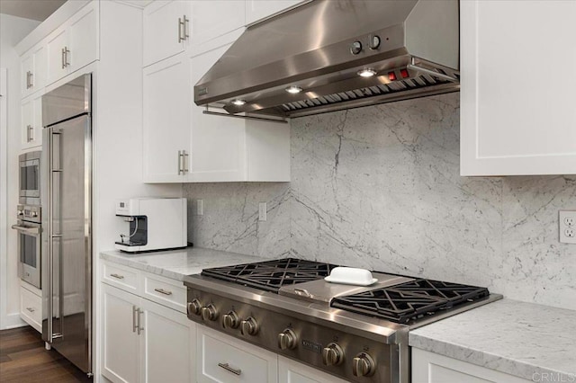 kitchen with white cabinets, tasteful backsplash, built in appliances, and under cabinet range hood
