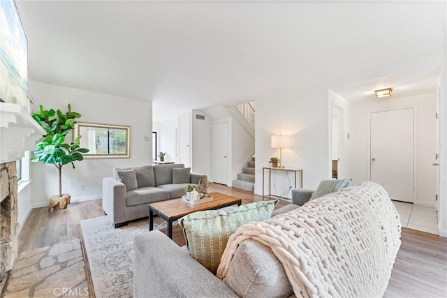 living area featuring light wood-style floors, stairway, a stone fireplace, and baseboards