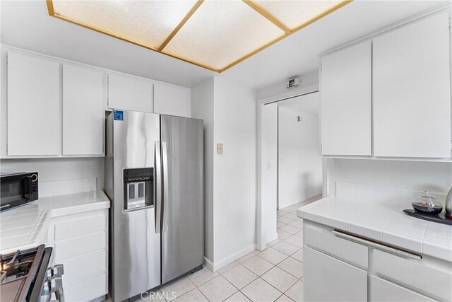 kitchen featuring light tile patterned flooring, tile countertops, baseboards, white cabinets, and appliances with stainless steel finishes