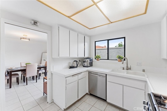kitchen with light tile patterned floors, white cabinets, a sink, tile counters, and stainless steel appliances