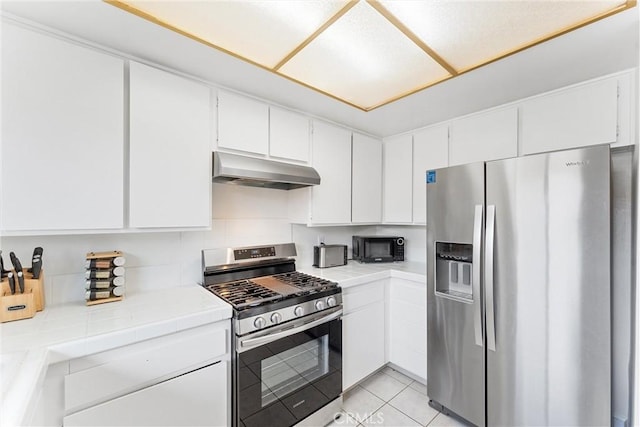 kitchen with light tile patterned floors, white cabinets, stainless steel appliances, under cabinet range hood, and tile countertops