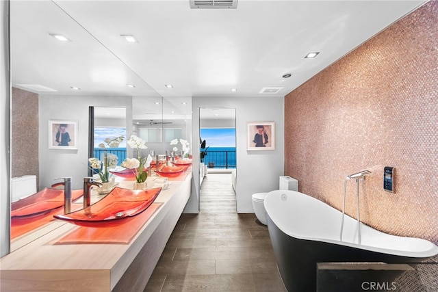 full bath with recessed lighting, double vanity, a soaking tub, and visible vents