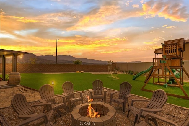 patio terrace at dusk with a fire pit, a yard, a fenced backyard, and a playground